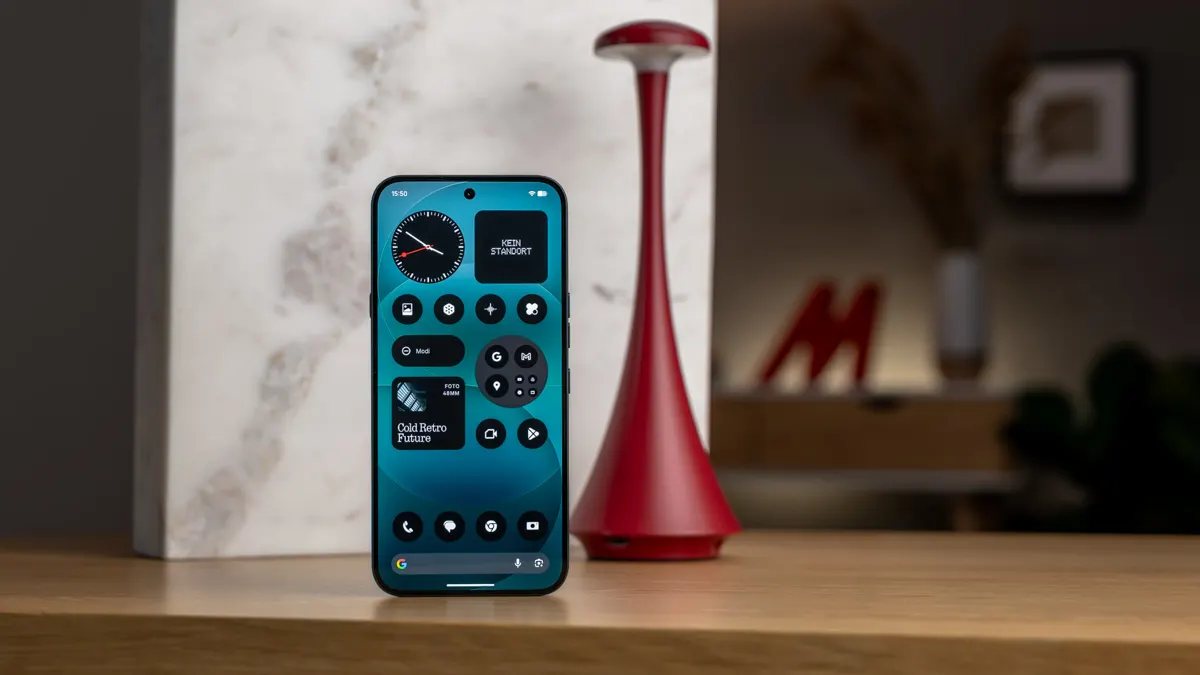 Das Nothing Phone (4a) Pro steht mit eingeschaltetem Display auf einem Tisch vor einer Marmorplatte und einer Tischlampe.