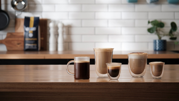 Verschiedene Kaffeegetränke in Gläsern und Tassen auf einer Küchenarbeitsplatte.