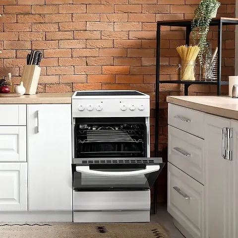 Μια κουζίνα με τοίχο από τούβλα δείχνει μια λευκή κουζίνα με ανοιχτή πόρτα, πλαισιωμένη από λευκά ντουλάπια και ένα ράφι.