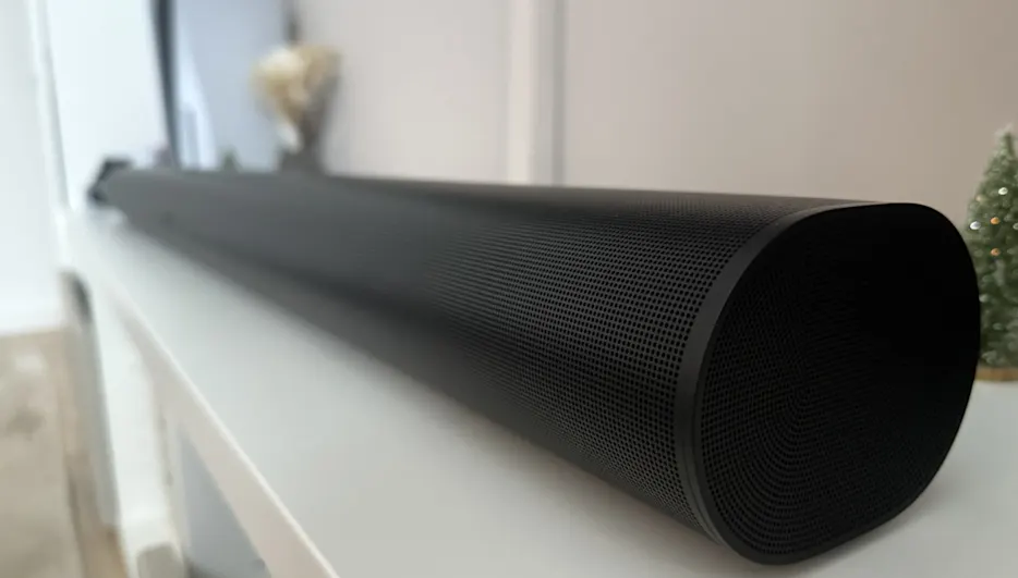 Ein schwarzer Lautsprecher liegt auf einer weißen Oberfläche. Im Hintergrund sind ein Fenster und eine kleine Dekoration zu sehen.