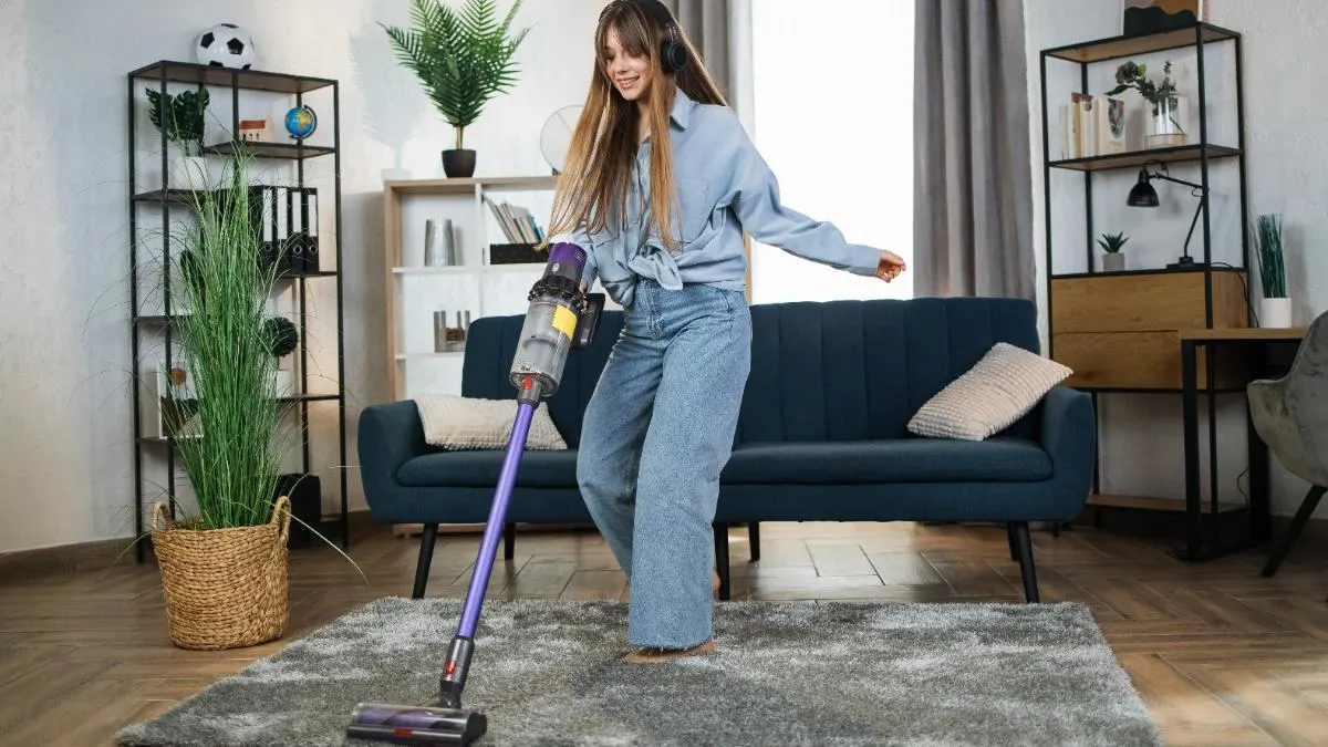 Eine Frau staubsaugt im Wohnzimmer auf einem Teppich und trägt dabei Kopfhörer.