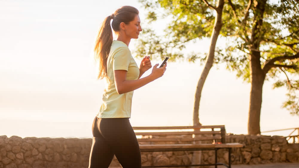 Eine Frau joggt mit einem Smartphone in der Hand.