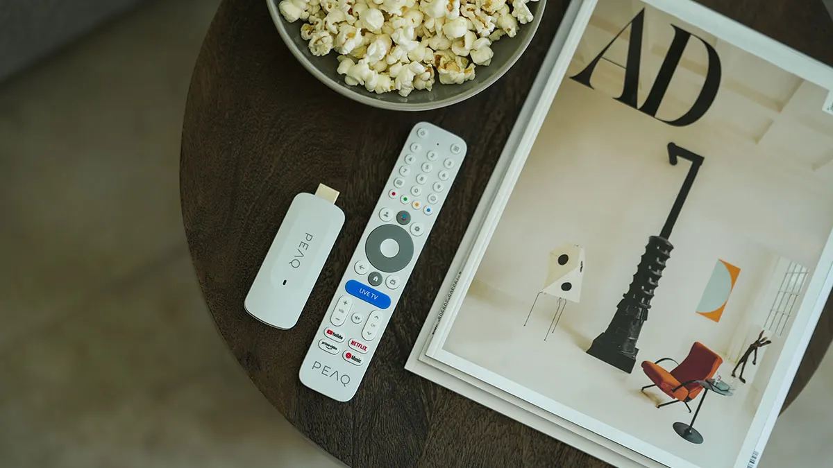 Der PEAQ PGS 4000 TV-Stick und seine Fernbedienung liegen auf einem Tisch neben einer Schale Popcorn und einer Zeitschrift.