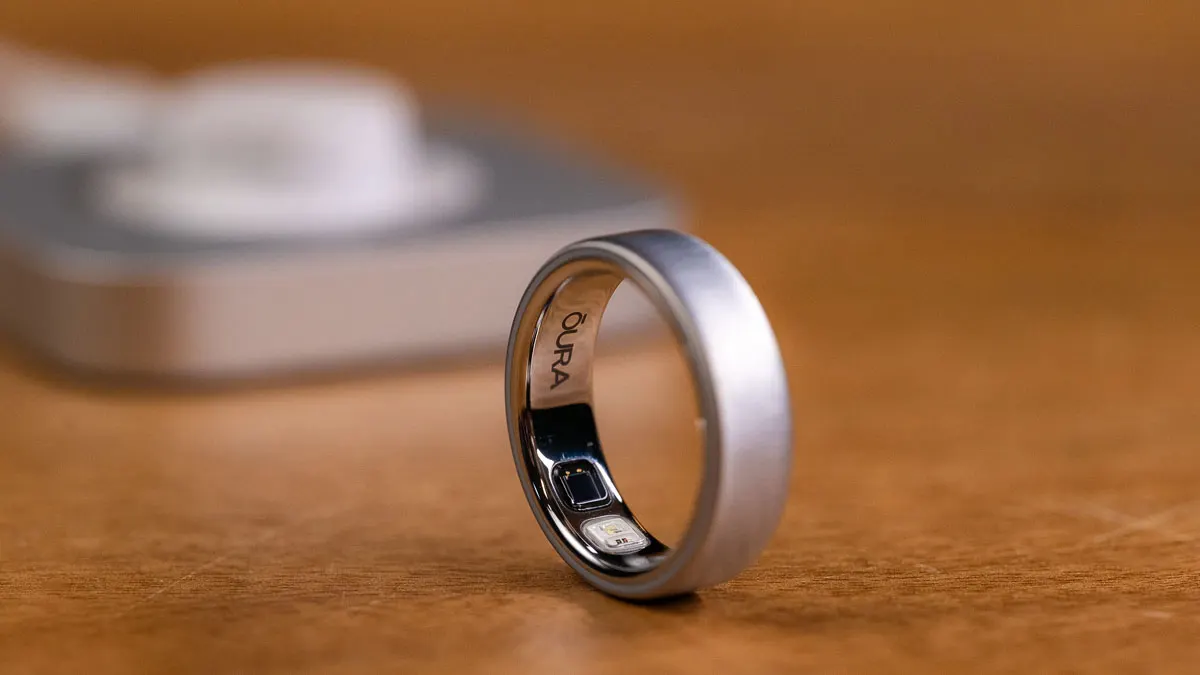 Der Oura Ring 5 steht auf einem Holztisch, im Inneren sind die Sensoren und der Oura-Schriftzug zu sehen.