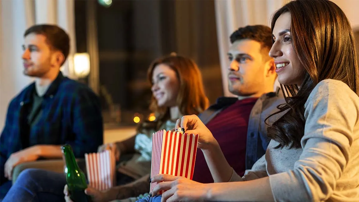 Vier Personen auf einer Couch essen Popcorn aus gestreiften Bechern und schauen in eine Richtung. 