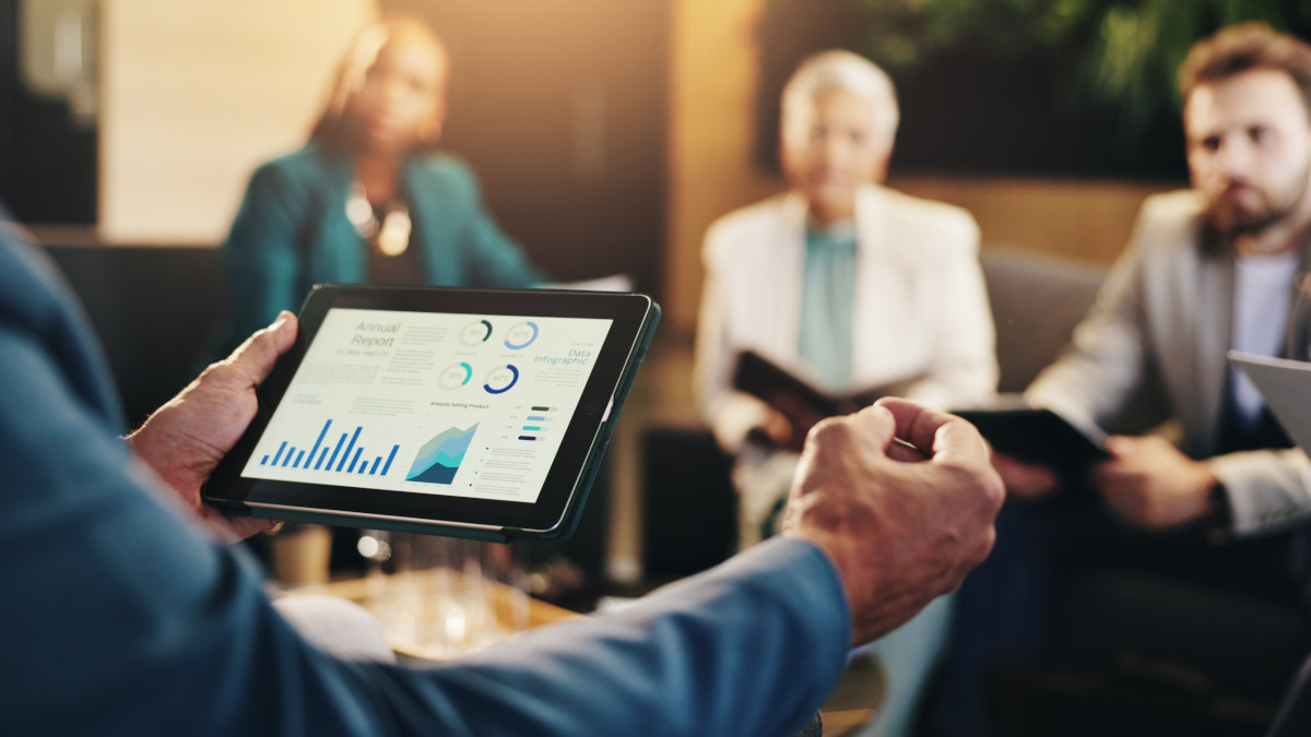 Geschäftsleute in einer Besprechung mit Tablet-Bildschirm. Darauf sind Daten und Diagramme zu sehen.