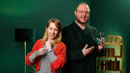 Franzi zeigt auf ihre Smartwatch und Andreas auf sein Smartphone.