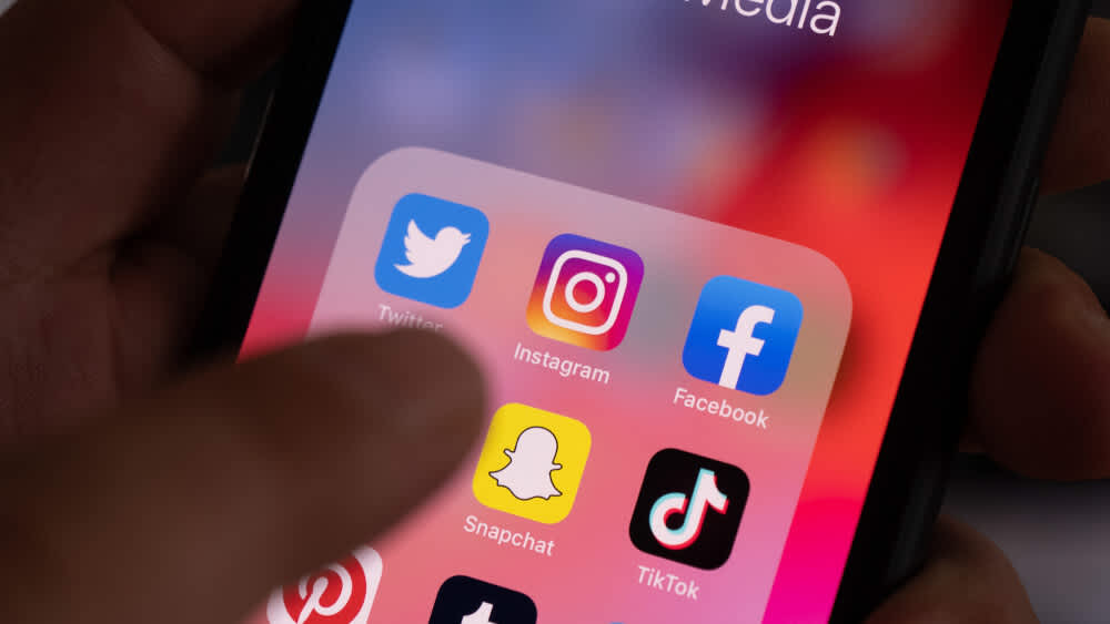 Ein Mann bedient ein iPhone, auf dem viele Social-Media-Apps runtergeladen sind.
