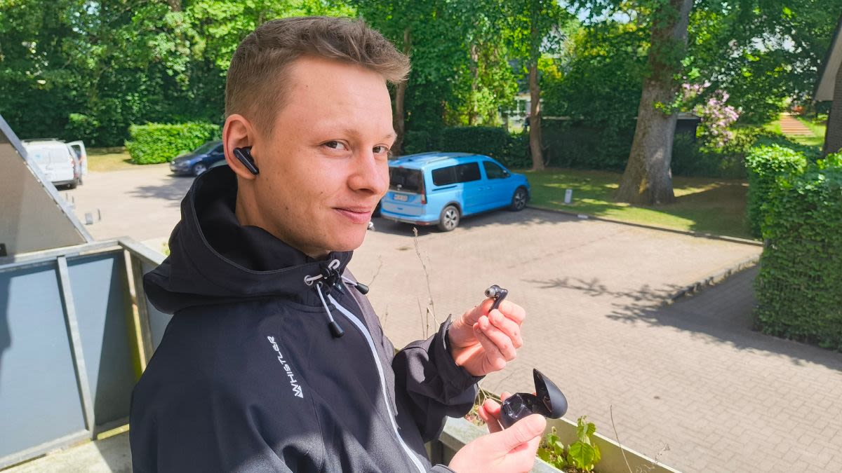 Alex steht draußen und trägt In-Ear-Kopfhörer.