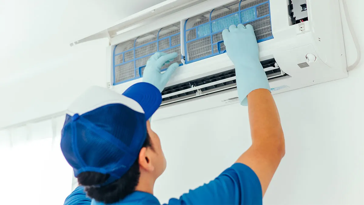 Eine Person mit Schutzhandschuhen reinigt eine Klimaanlage.
