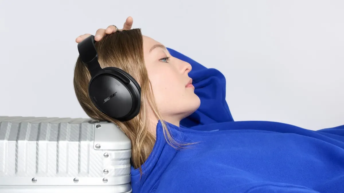 Eine Frau trägt den Bose QuietComfort Kopfhörer (2. Gen.) und lehnt ihren Kopf gegen einen Koffer.