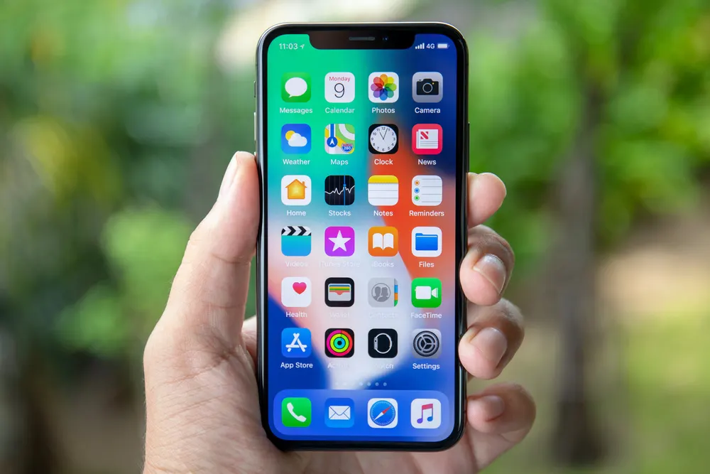 Eine Hand hält ein Smartphone mit bunten App-Symbolen auf dem Bildschirm vor einem grünen Hintergrund.