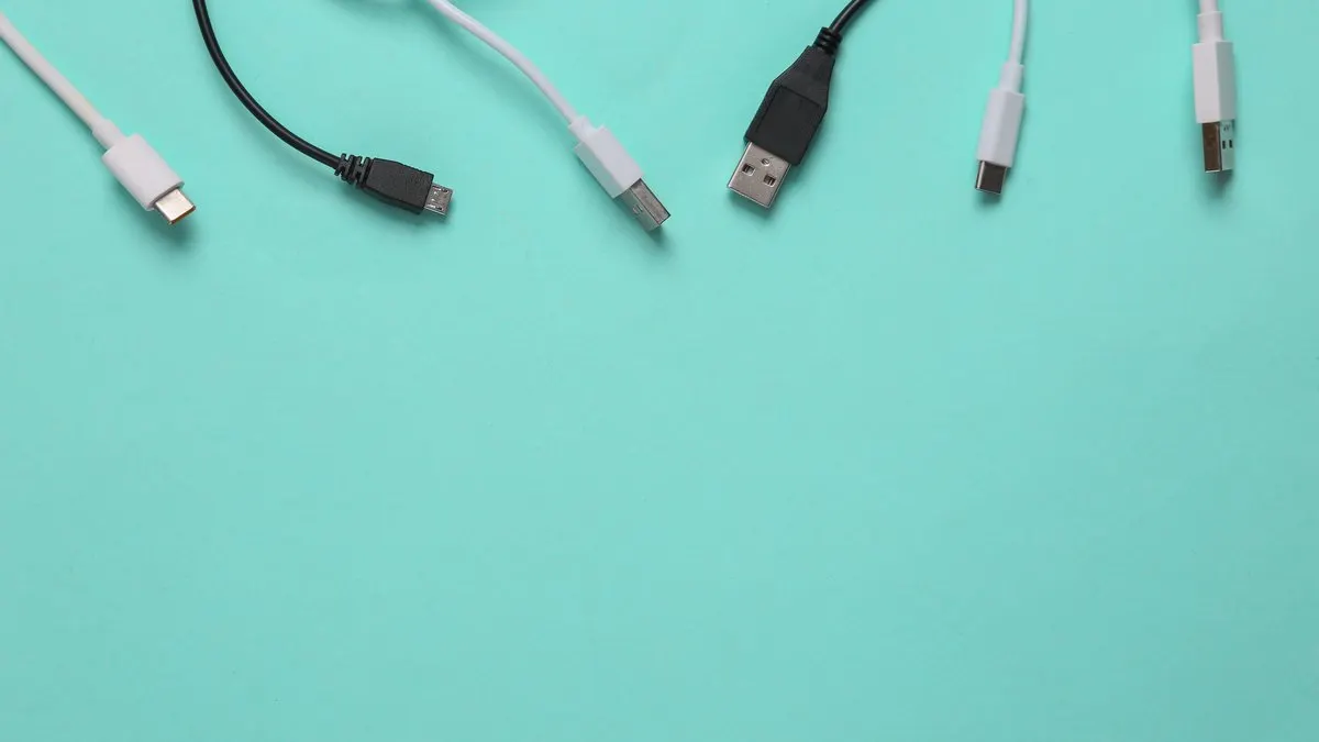 Auf hellblauem Grund liegen Kabel mit USB-, USB-C- und Micro-USB-Anschlüssen in Weiß und Schwarz.