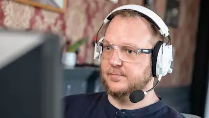 Andreas mit dem Razer BlackShark V3 Pro auf dem Kopf schaut auf einen Monitor.