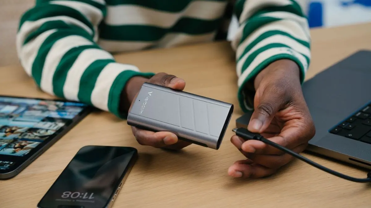 Eine Frau koppelt die externe SSD Verbatim TurboMetal mit einem Laptop. Neben ihr liegen ein Tablet und ein Smartphone.