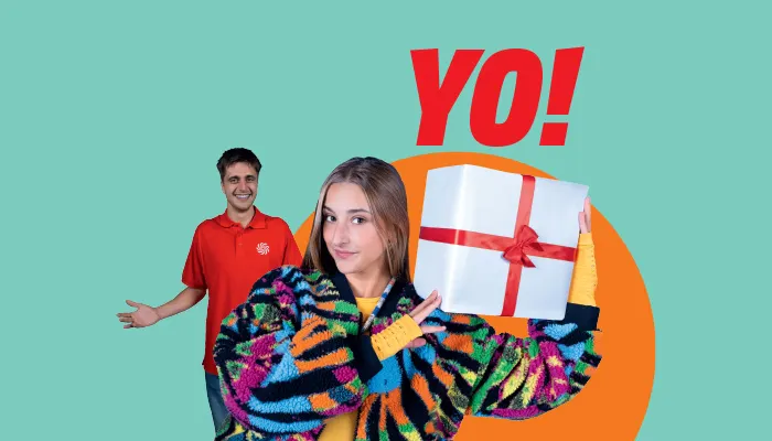 YO!“-Schriftzug auf türkisgrünem Hintergrund: vorne Kunde im bunten Pullover hält Geschenk mit roter Schleife, MediaMarkt-Mitarbeiter im Hintergrund.