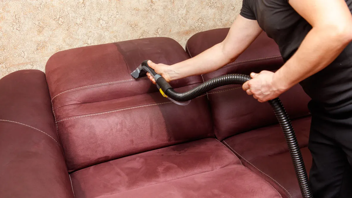 Ein Mann reinigt ein Sofa mit einem Waschsauger.