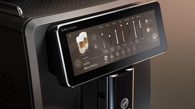 Nahaufnahme einer Kaffeemaschine mit Touchscreen-Bedienfeld zur Auswahl von Getränken und Einstellungen.