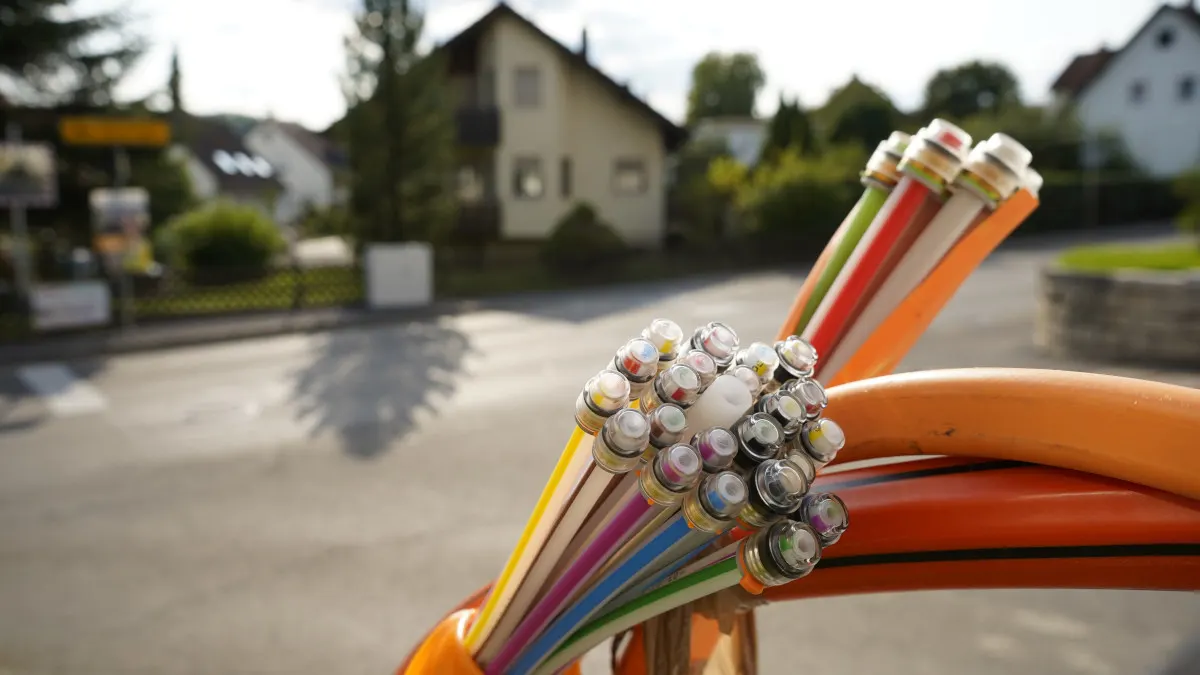 Glasfaserkabel in der Nahaufnahme vor einer Wohnsiedlung im Hintergrund.