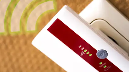 Ein weißer WLAN-Verstärker mit rotem Streifen ist in eine Steckdose gesteckt. Grüne LED zeigen Betrieb an. WLAN-Symbol links.