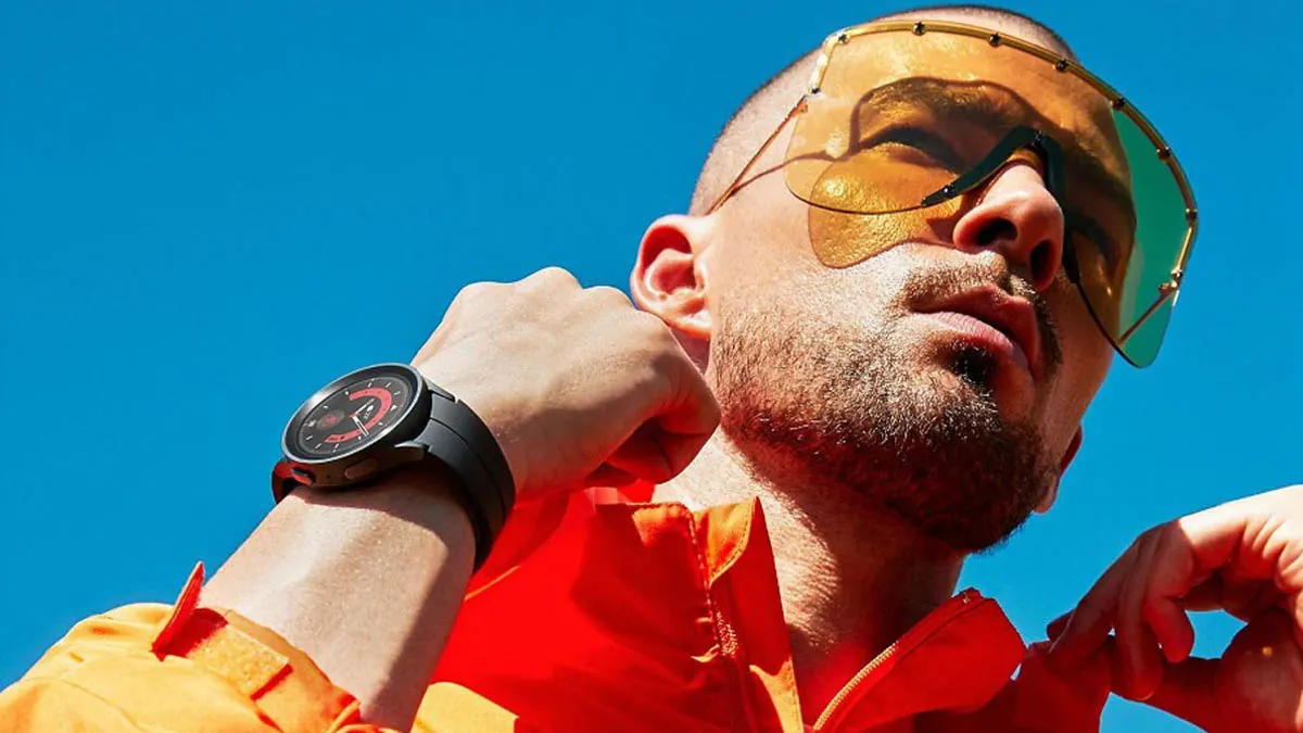 Mann mit gelber großer Sonnenbrille und orange-roter Jacke richtet sich den Kragen. An einer Hand sieht man die Samsung Galaxy Watch 5 Pro.