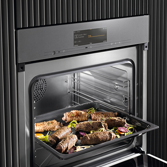 Ein Ofen mit einem Display zeigt eine Metallschale mit Rouladen und Gemüse. Metallstäbe sind im Ofen sichtbar.