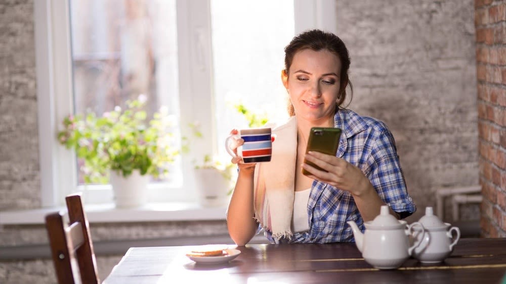 Frau sitzt mit Kaffee und Smartphone am Tisch