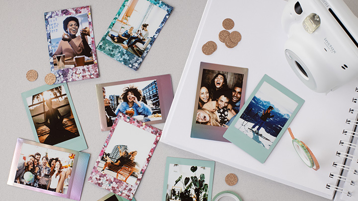 Auf einem Tisch liegen Fotos, eine Kamera und ein Notizbuch. Die Fotos zeigen Menschen und Landschaften. Runde, braune Konfetti sind verstreut.