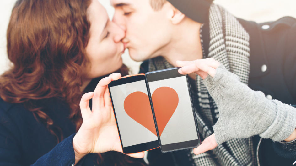 Küssendes Paar hält Smartphones mit Herzgrafik aneinander