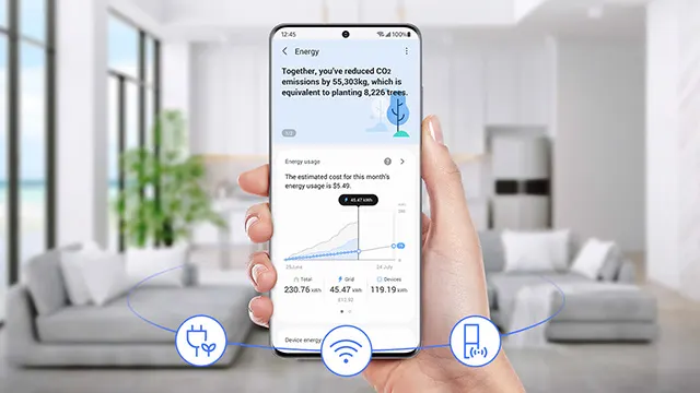 Hand hält Smartphone mit Energie-App vor Wohnzimmer. App zeigt CO2-Reduktion und Energieverbrauch an. Sofa und Pflanze im Hintergrund.