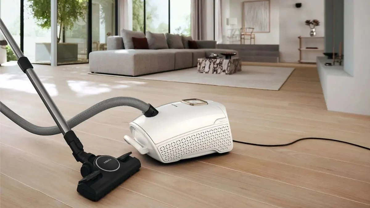 Der Staubsauger Miele Guard L1 Performance steht auf einem Parkettboden in einem Wohnzimmer.