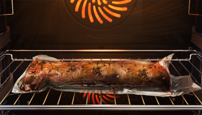 Ein Braten auf Backpapier liegt im Ofen auf einem Rost. Das Heizelement ist orangefarben.