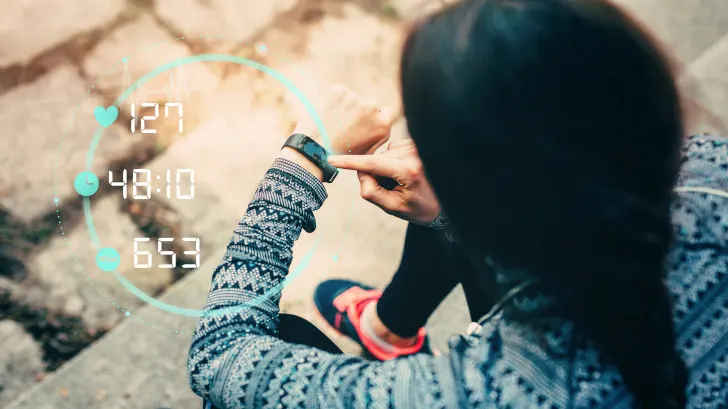 Frauenhand tippt auf eine Smartwatch mit digitaler Anzeige von Herzfrequenz, Zeit und Schrittzahl auf einer Steintreppe.