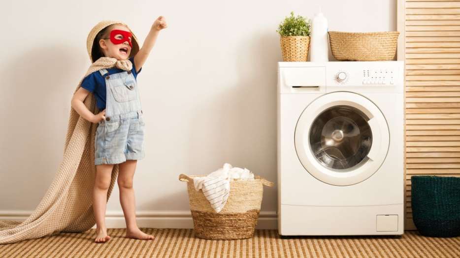 Ein als Superheld verkleidetes Kind steht neben einer Waschmaschine.
