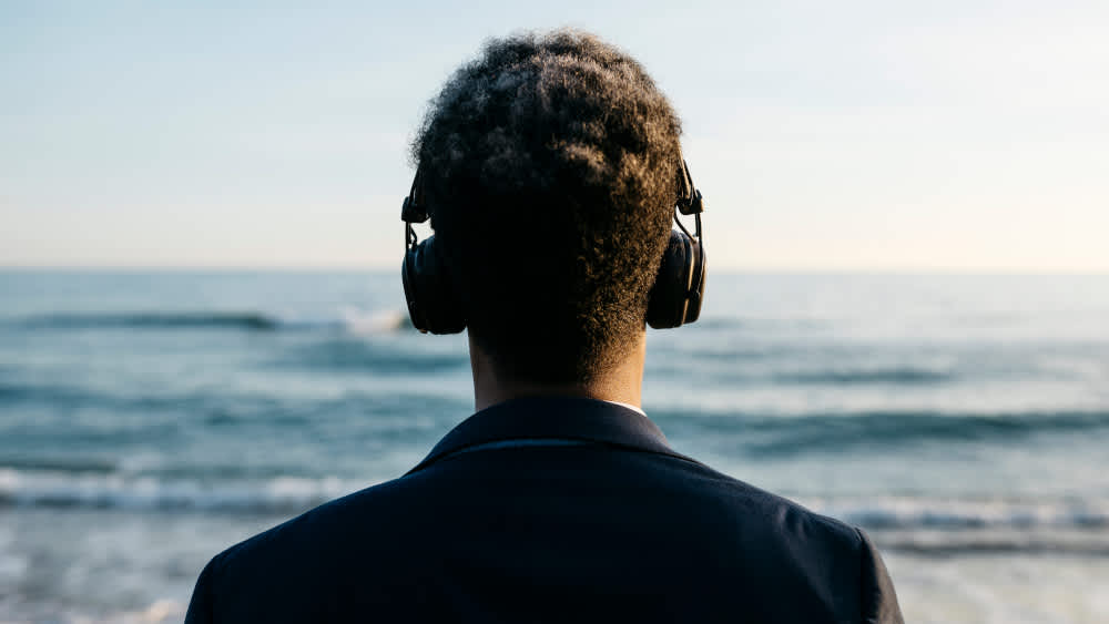 Ein Mann trägt Over-Ear-Kopfhörer am Meer.