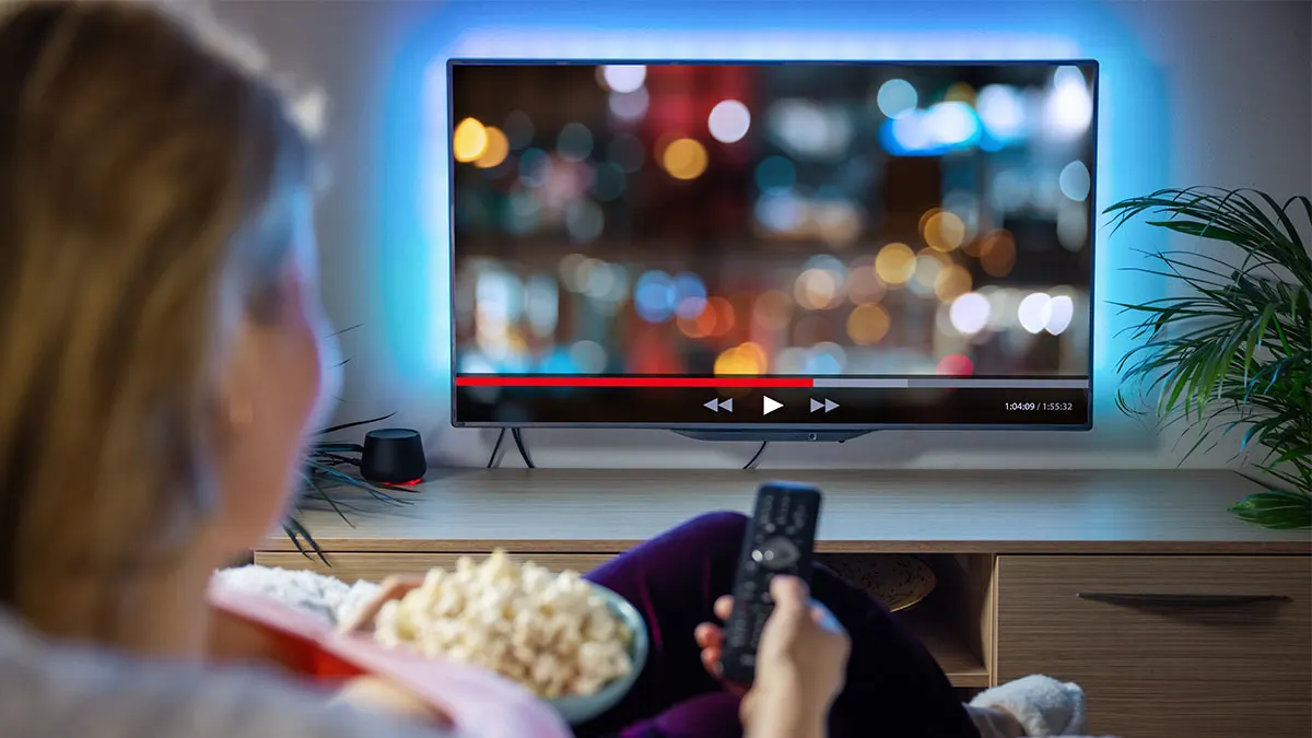 Frau sitzt mit Popcorn vor dem Fernseher und hält eine Fernbedienung in der Hand.