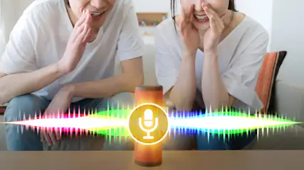 Zwei Personen sitzen mit einem Lautsprecher auf einem Sofa, der ein Mikrofonsymbol anzeigt.