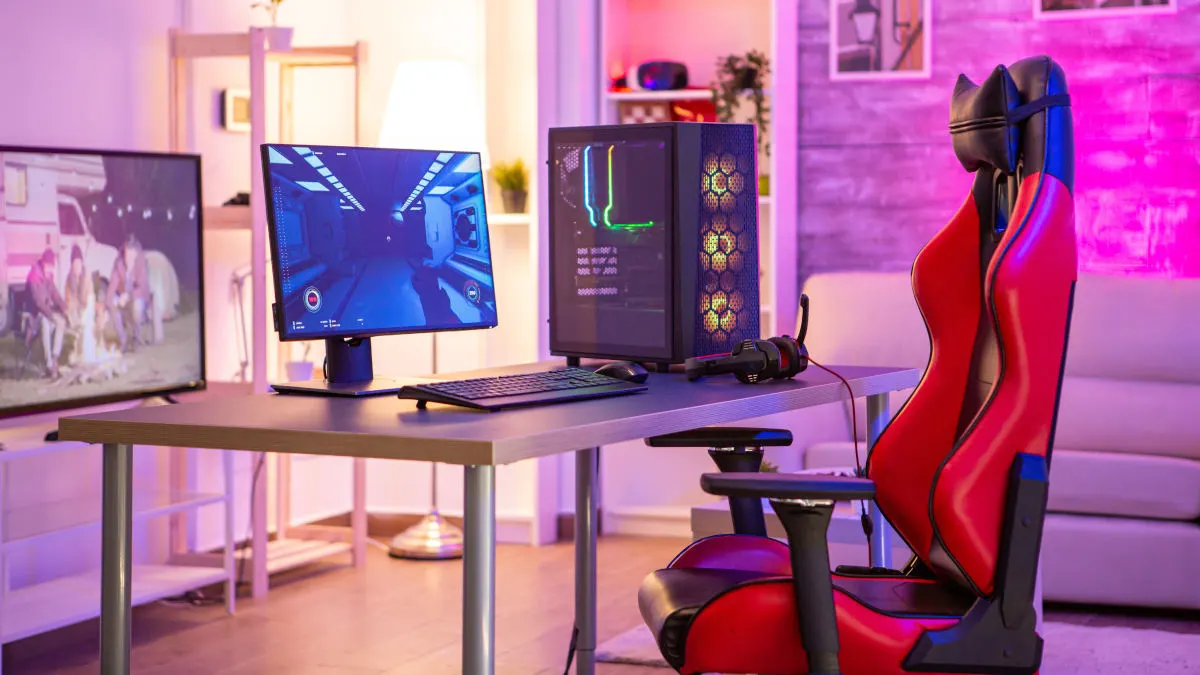 Ein rot-schwarzer Gaming-Stuhl steht vor einem Schreibtisch mit einem PC-Gaming-Set-up. (Adobe Stock Dateinr.: 315314598)