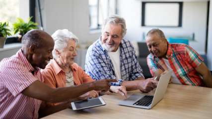 Eine Gruppe von älteren Menschen schaut sich gemeinsam etwas auf einem Laptop an.