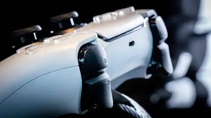 Nahaufnahme eines weißen Spielecontrollers mit schwarzen Knöpfen vor einem dunklen Hintergrund.