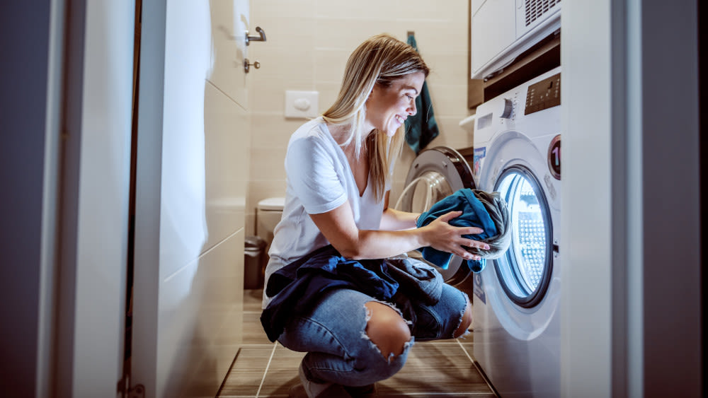 Lächelnde Frau kniet neben Waschtrockner