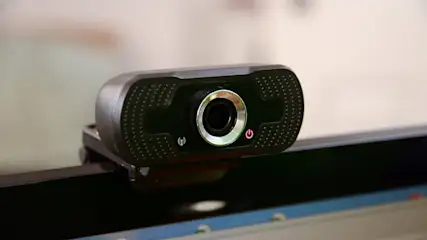 Eine schwarze Webcam ist an einem Monitor befestigt. Sie hat ein silbernes Objektiv und Knöpfe für Strom und WLAN.