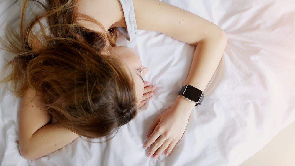 Eine Frau schläft ein einem Bett mit einem Schlaftracker am Handgelenk
