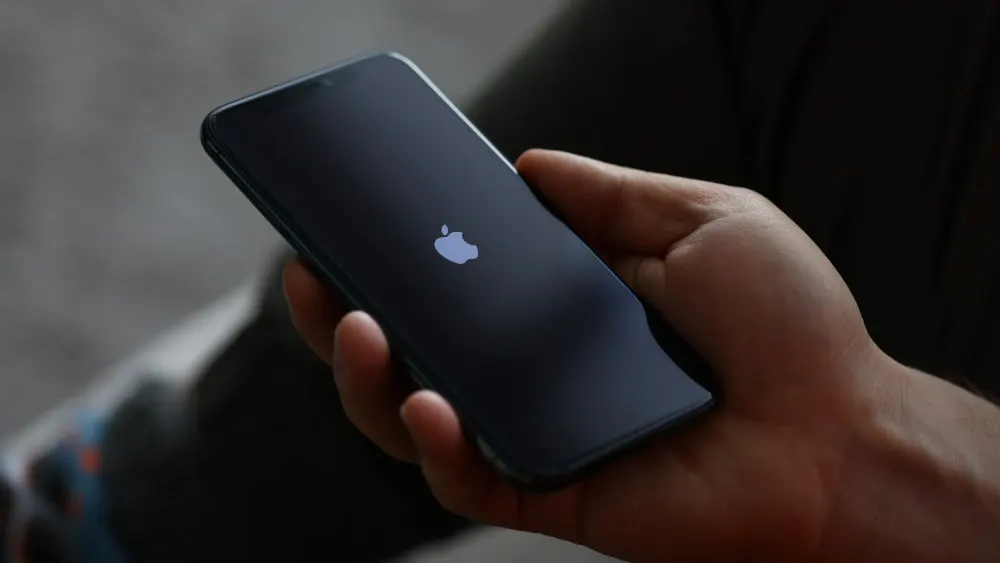 Eine Hand hält ein schwarzes Smartphone mit einem hellen Apfel-Logo auf dem Display.