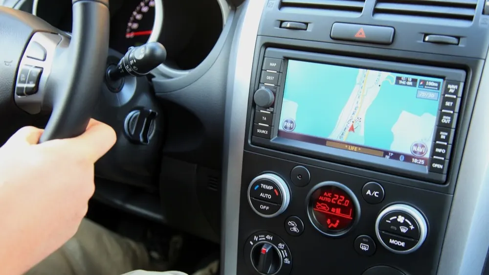 Innenraum eines Autos mit sichtbarem Lenkrad, Navigationssystem und Bedienelementen für Temperatur und Lüftung.