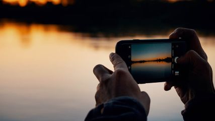 Mann fotografiert Wasser und Sonnenuntergang mit einem iPhone.