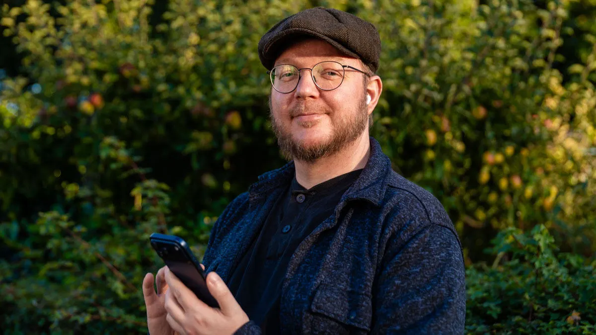 Andreas ist draußen in der Natur unterwegs, trägt die AirPods Pro 3 in den Ohren und hält das iPhone 17 Pro Max in der Hand.