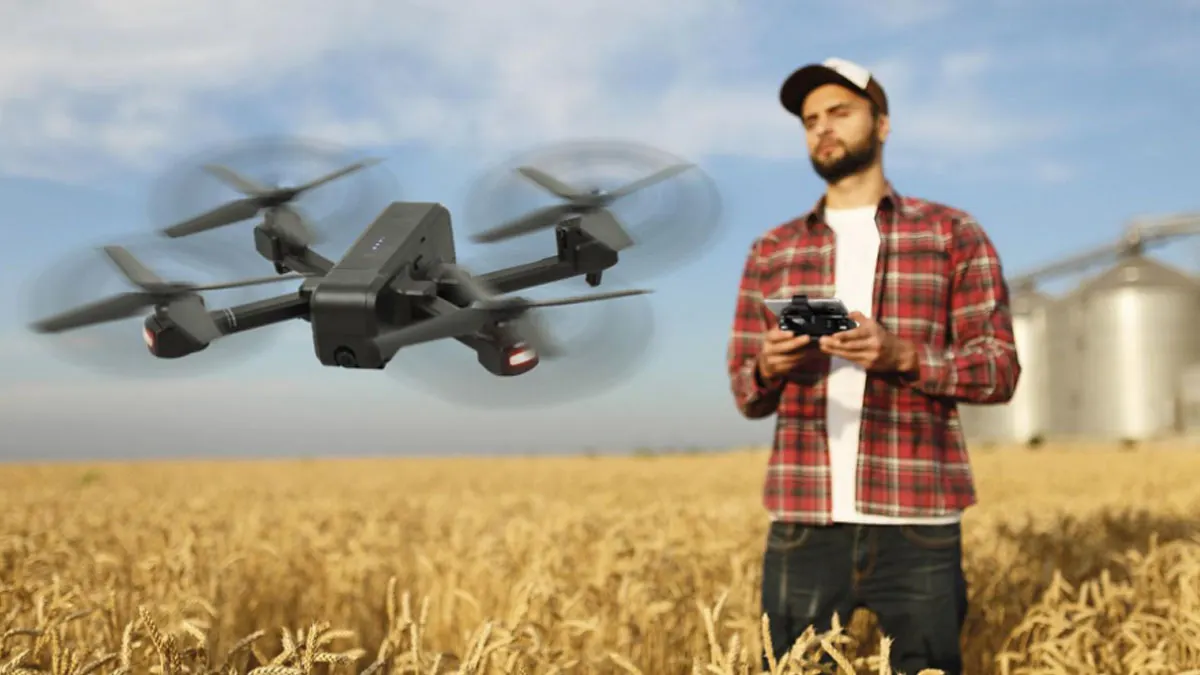 Ein Mann hält eine Steuerung für eine Drohne über einem Feld und einem bewölkten Himmel im Hintergrund.