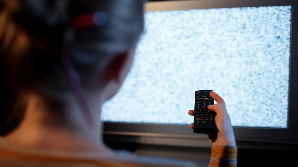 Eine Frau sitzt mit einer Fernbedienung vor einem Fernseher mit Bildstörung.