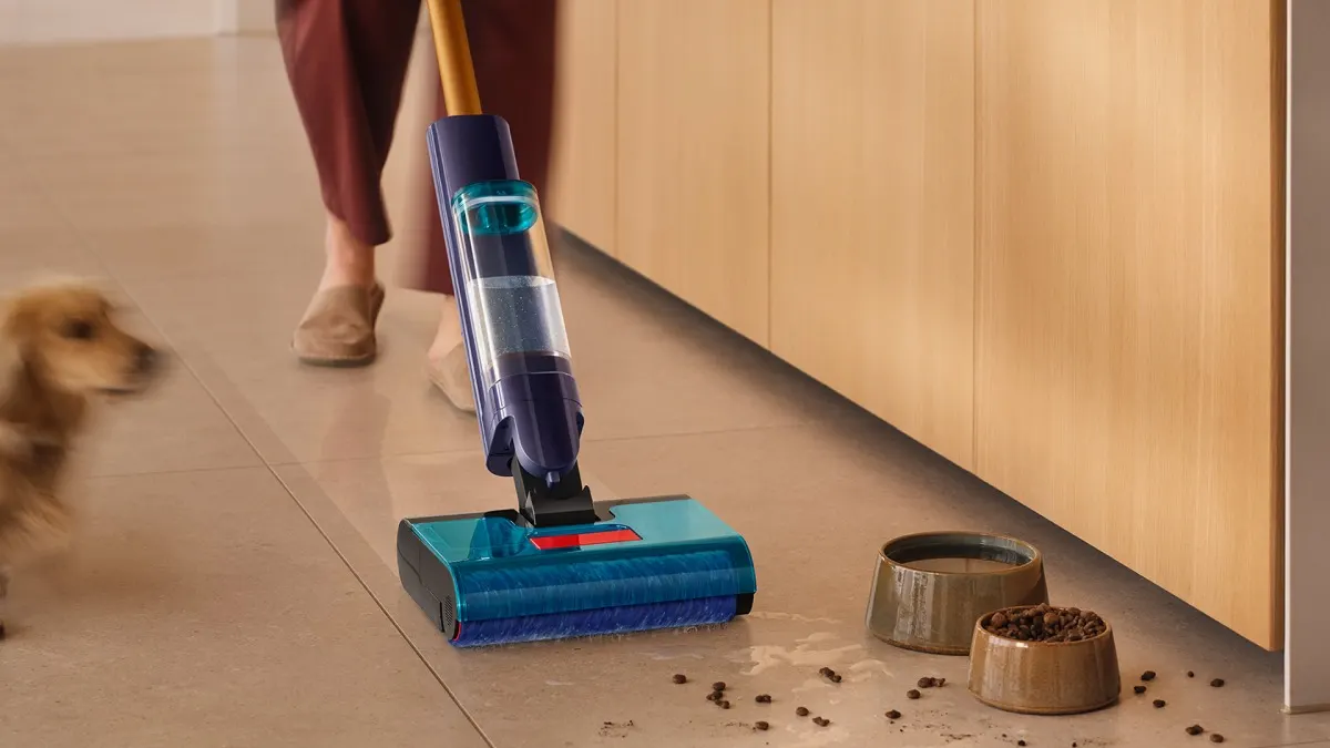Eine Person saugt verschüttetes Trinkwasser und Hundefutter neben zwei Näpfen mit dem Dyson Clean+Wash Hygiene. Links erkennt man einen Hund.
